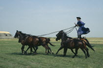 Cossack horseman driving team of five horses from sanding position on backs of pair behind.