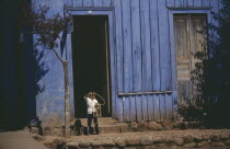 Young child standing in doorway of blue painted building swinging lasso.