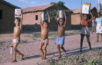 Group of young children of mixed race carrying water in various metal containers on their heads in slum area.Brasil shanty favela Brazil
