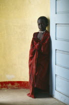Masai child standing between yellow wall and blue door.  The Masai have been expelled from the Ngorongoro Crater area to make way for tourists and wildlife.