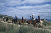 Tourist group trekking on horseback through rural landscape.