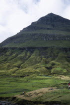 People working in hay field on lower slopes of steep pointed hillside.