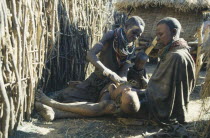 Female witch doctor or Amuron using sysal to suck out evil from child affected by the evil eye.  Karamojong women paint their faces with clay to prevent disease.Pastoral tribe of the Plains Nilotes g...