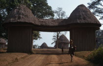 Thatched gateway with woman and children below.