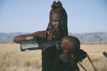 Himba woman giving child a drink of water from Coca Cola bottle.  The Himba traditional way of life is being threatened by uncontrolled tourism.Semi nomadic pastoral people related to the Herero and...
