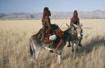 Himba women and child on donkeys in grassland area. Semi nomadic pastoral people related to the Herero and speaking the same language
