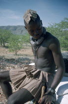 Kaokoland.  Himba man sitting on bumper of safari jeep.  Cloth covering head denotes that he is married. Semi nomadic pastoral people related to the Herero and speaking the same language