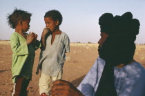 Tuareg man looking towards two children.Minority nomadic people of Berber origin cheche toureg