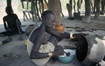 Young Dinka woman ladelling the oil produced from shea butter fruit after roasting and boiling which is used for cooking and body decoration.
