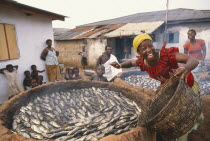 Smiling woman smoking fish in large  circular clay oven.