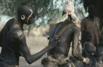 Dinka tribesman painting the back of another with dung ash.