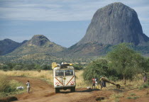 Minibus travelling along dirt road with people at the side