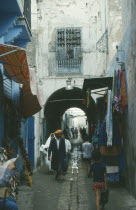 Market scene.  Men and children walking through narrow cobbled street lined with shops.