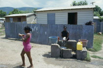 Bower Bank Transit Camp.  Girls beside water pipe with simple housing behind.