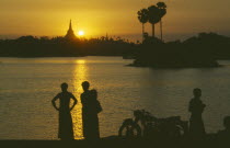 People silhouetted on shore of lake looking across towards the Shwedagon Pagoda at sunset.Burma Myanmar  Rangoon Shwe Dagon