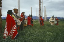 Native Indian Kwakiutl tribe totem poles with tribesmen and a dancer dressed as an animal deity