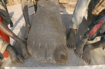 Boys playing in Managa Sculpture park on the outskirts of Ouga.  Cropped view of their feet as they stand beside the huge stone foot of a sculpture.