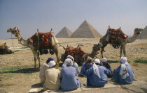 Group of men with camels and the Pyramids behind.