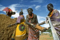 Brightly dressed Karamojong women making bricks. Blue sky behind.