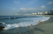 Ipanema Beach with bathers standing at the waters edge in early morning light with misty mountains in the distance.Brasil Brazil