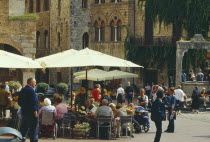 Street scene with people sitting at outside tables of busy cafe with sun umbrellas.