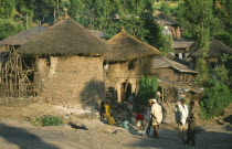 Two storey  circular stone buildings with thatched rooftops  unique to the area.  Villagers and children on road outside.