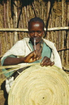 Woman making circular mat from straw  stitched into place.