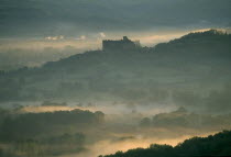Castelnau-Bretenoux Castle silhouetted on hillside against pale  misty sky.