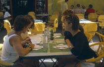 Arles.  Le Cafe La Nuit  Place du Forum.  Four young women seated at a table reading a menu.