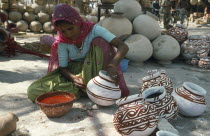 Local woman in sari decorating pots by hand with red paint.