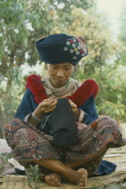 Yao Tribeswoman making clothes for young adult.