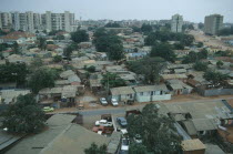 Cars parked next to houses along a road with high rise apartment blocks in the distance.