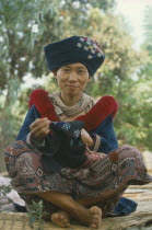 Yao Tribeswomen sitting on ground making clothes for young female adult.