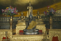 Wat Pho. Detail of Golden Buddha shrines on red and gold table with flower pots either side.