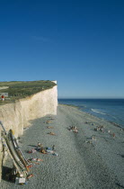 View across occupied peeble beach with boat leaning against a section of cliff face.