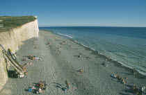 View over occupied peeble beach with boat leaning against cliff face.