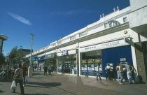 Busy pedestrian shopping area with people using cash machines.
