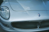Detail of silver Maserati with emblem and front light.