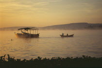 Uganda, Jinja, Golden sunrise over Lake Victoria. Boats silhouetted in foreground.