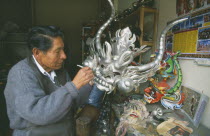 Man painting a large silver mask.