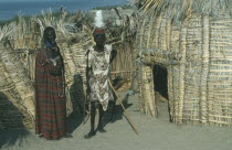 Turkana tribe  two men standing outside a traditional hut made from dry fan palm leaves.