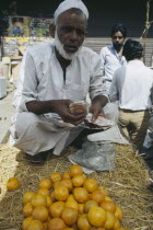 Man behind display of oranges on stall  crouching on ground holding money.transactiontransaction