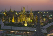 View over the Royal Palace complex and Temple of the Emerald Buddha at sunset with buildings illuminated against dusky pink sky.