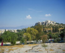 A road with trees either side in the foreground with the Acropolis up the hill.