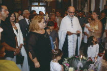 A Greek orthodox christening  The Priest reads with friends and family watching from behind.