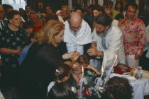 A Greek orthodox christening  the child being held and water poured over him with friends and family watching from behind.