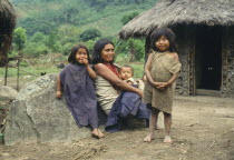 Kogi woman sitting on the ground with three children outside their thatched home