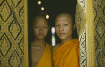 Two novice Buddhist monks framed in decorated doorway of wat.