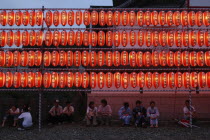 Festival goers at the Gion Matsuri rest under rows of illuminated chochin lanterns with name of donor to Narita san Temple written on each