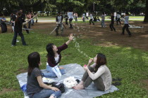 Harajuku. Yoyogi Park. Miki Tomiyoka  aged 23  blows bubbles for two friends while a group practices with swords in the background on a Saturday afternoon